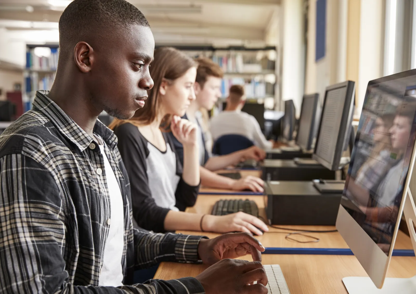 Library patrons working side by side at a row of public computer terminals.