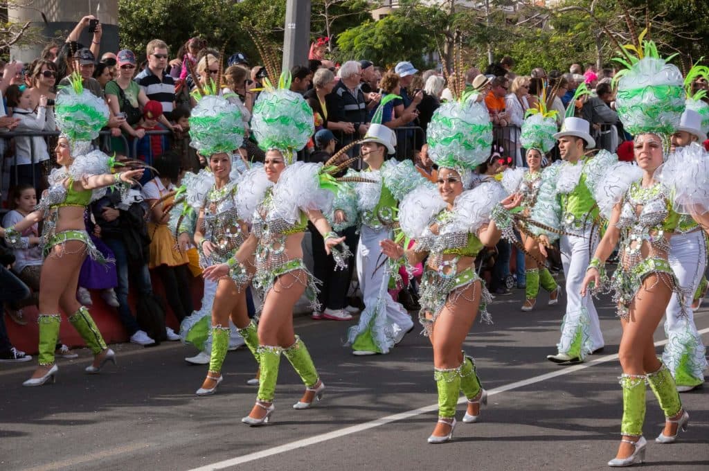 Dancers wearing colorful green outfits walking down a street parade in Tenerife