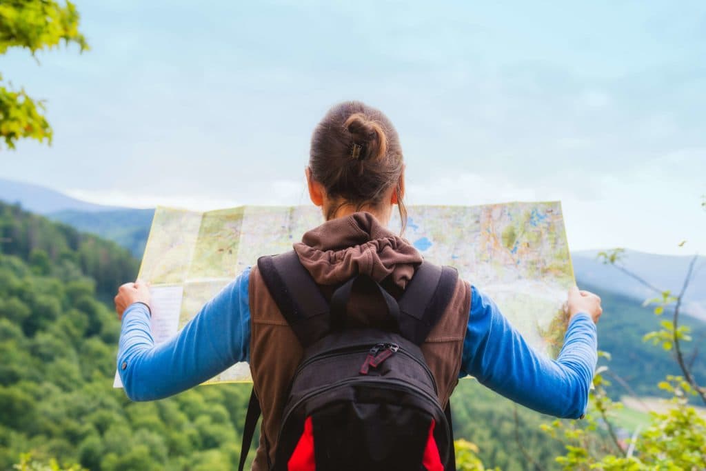 A young woman in a forest wearing a backpack looking at a map