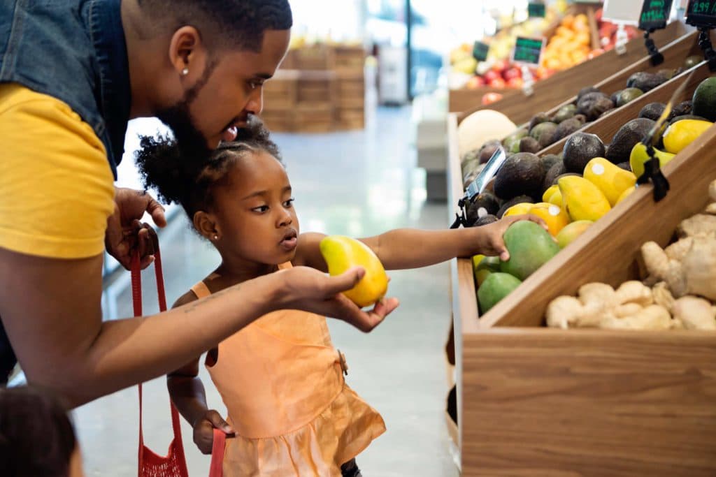 A father and daughter picking out mangos at the grocery store