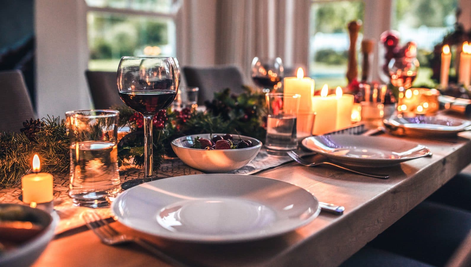 A beautiful dinner table decorated with candles, a wreath, and mistletoe