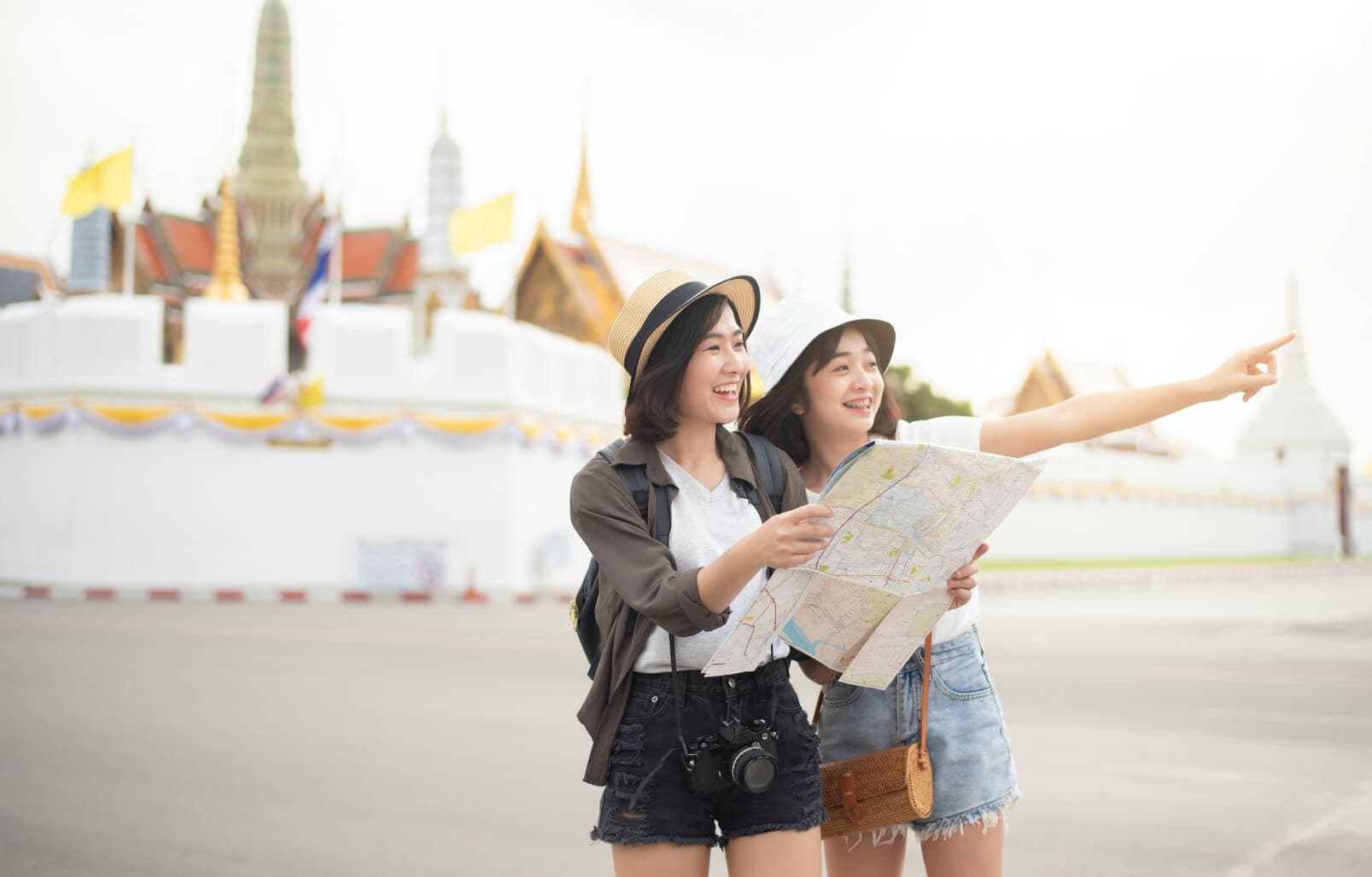 Two girls with a map, cameras, and sun hats touring a city