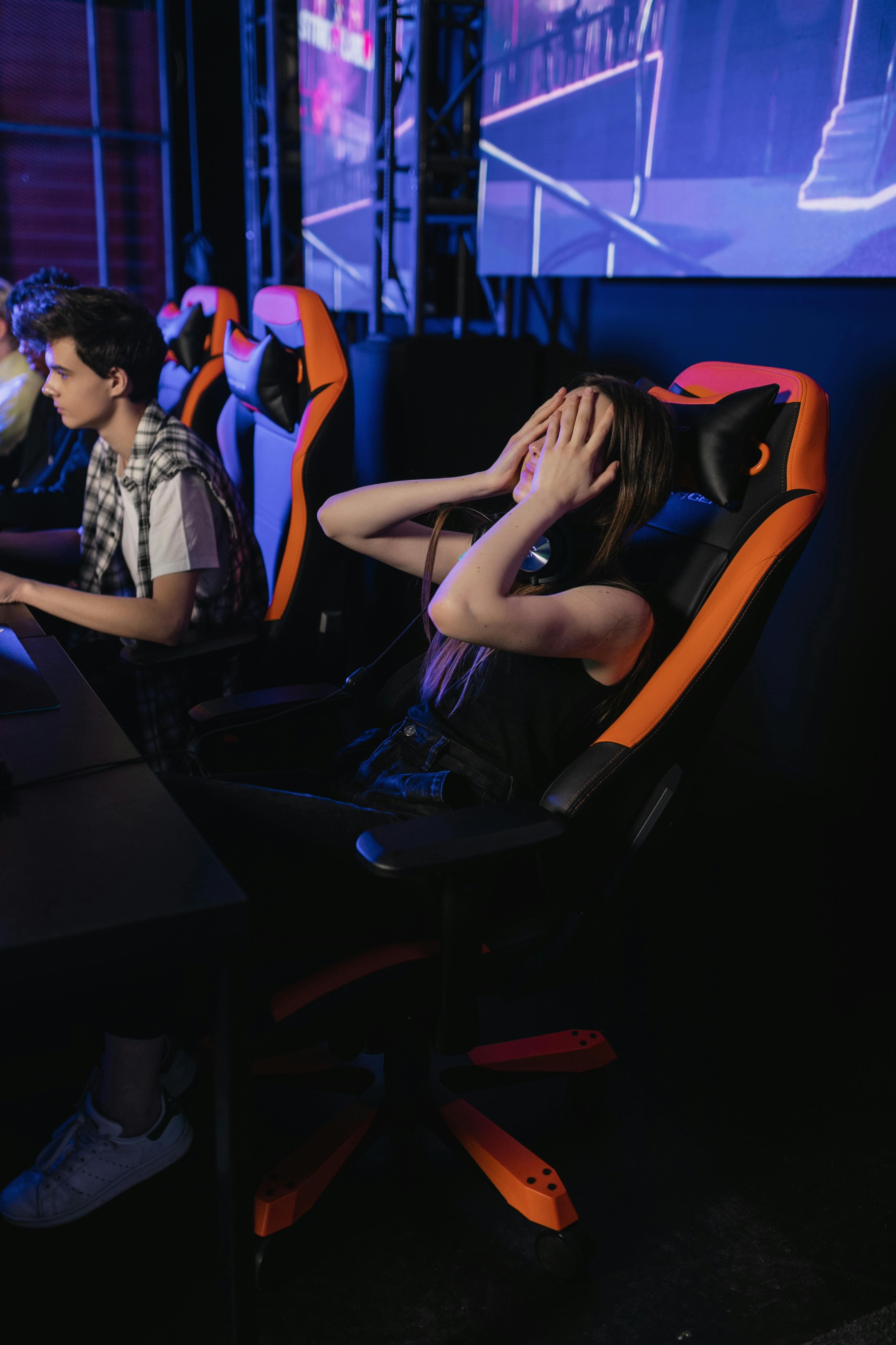 A photo of a woman in a red and black gaming chair. She is leaning back and placing both palms over her face, looking disappointed in herself.