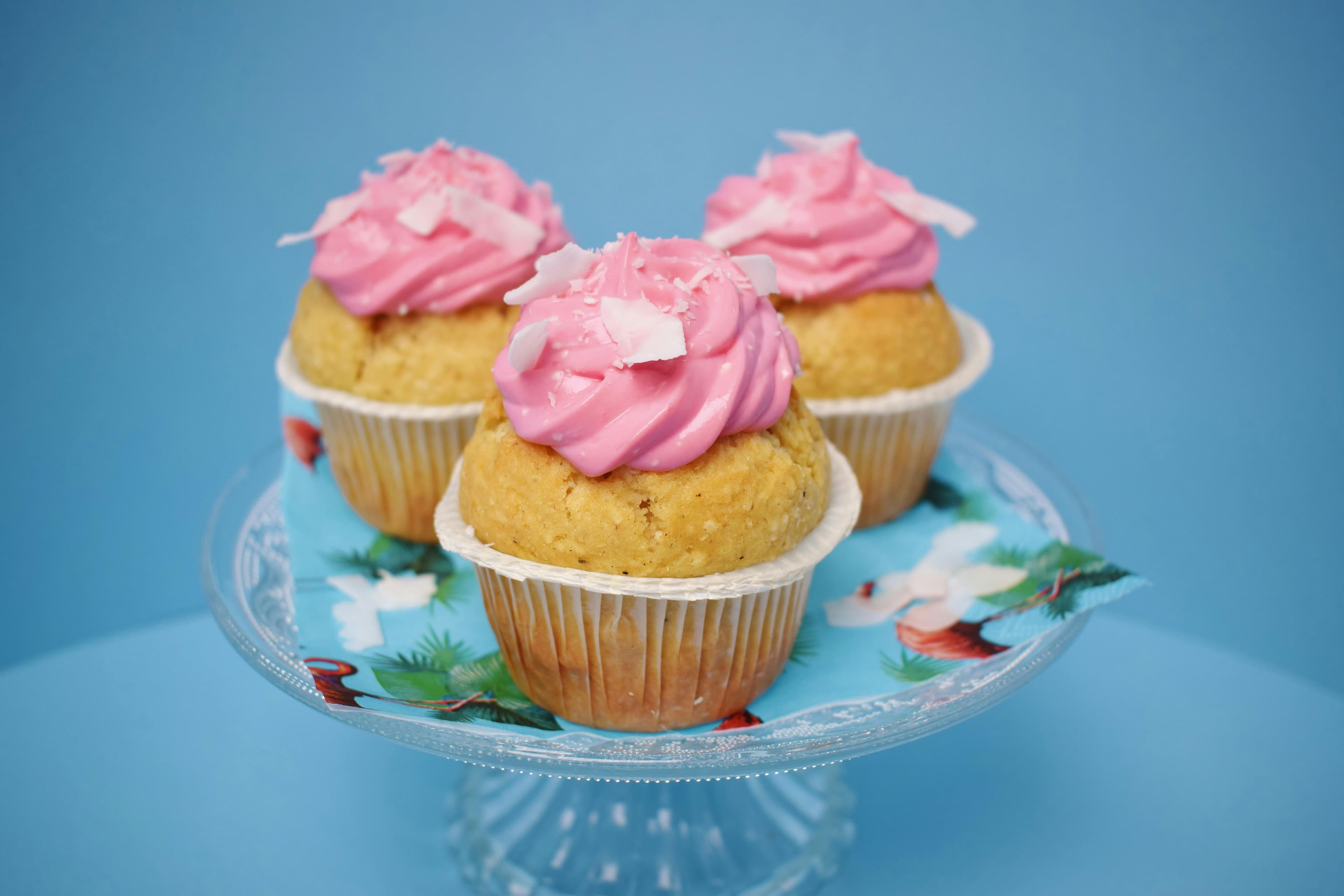 A glass platter containing three cupcakes with pink icing.