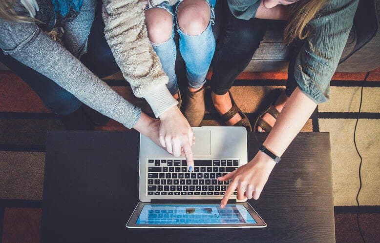 Three people all pointing at a computer screen while looking at something