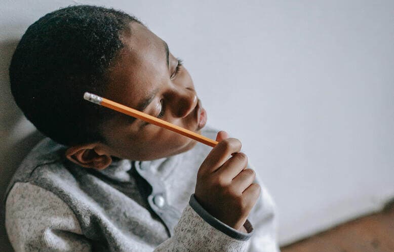 A young child holding a pencil thinking about something