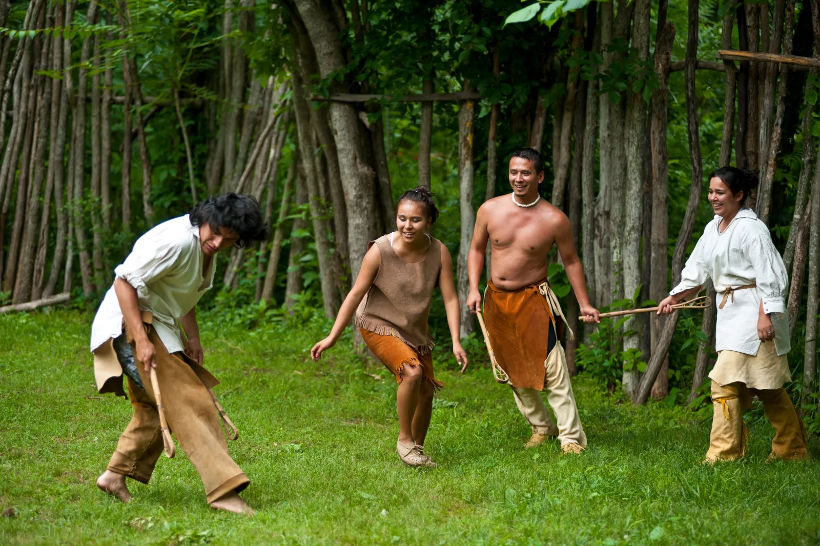 Cherokee players in traditional dress mid-game on a grass clearing at the treeline