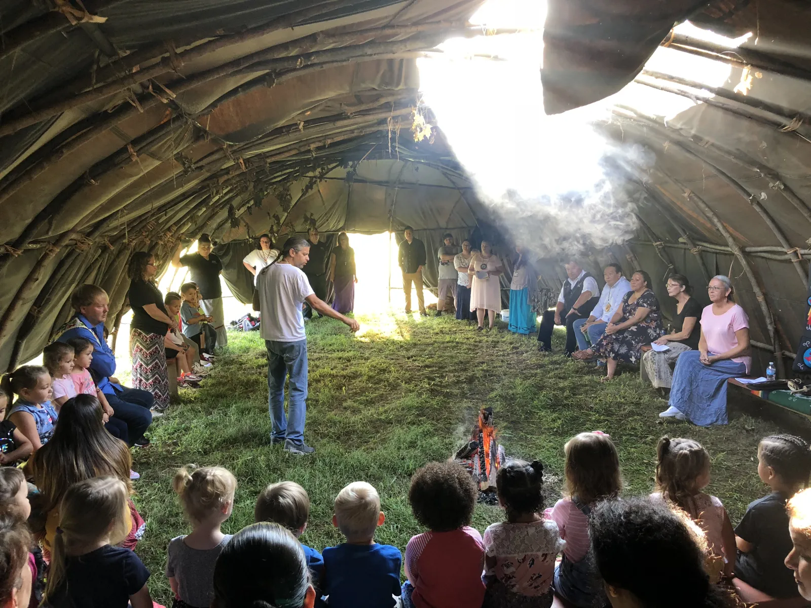 People gathered under a wooden arbour around a fire at a community event