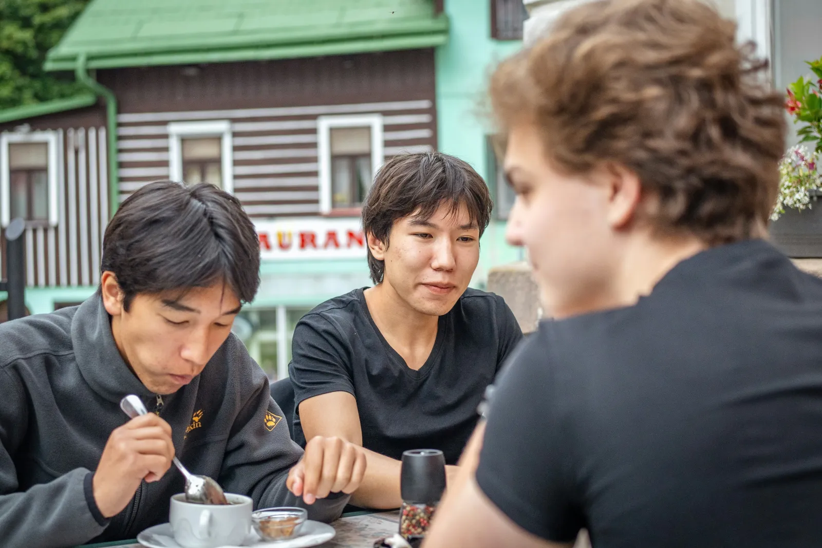Three friends eating together at an outdoor table, mid-conversation.