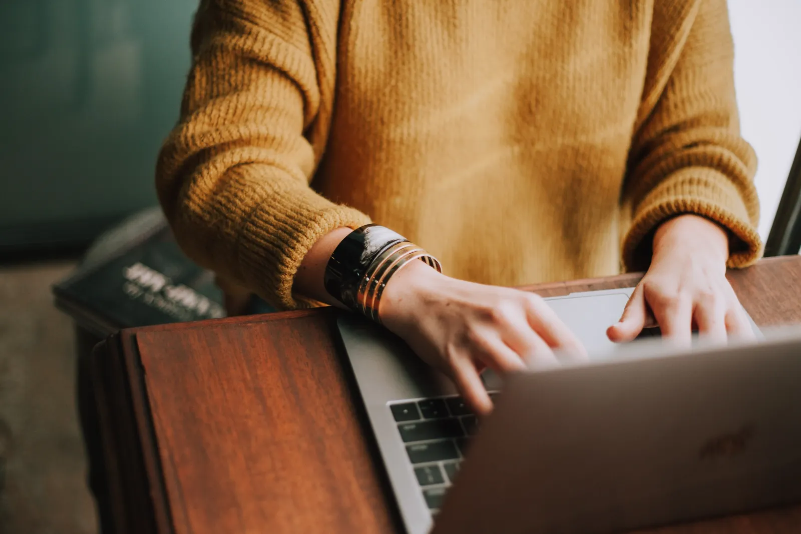 Close view of a person's hands typing at a laptop on a wooden desk.