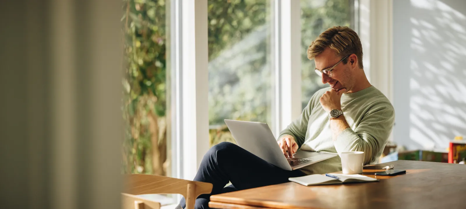 A man working at a laptop at a long window counter, plants along the sill.