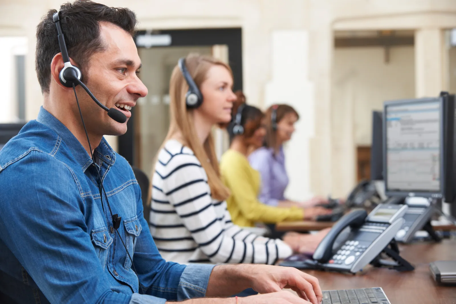 A row of agents in headsets working at desks along a call-centre bench.